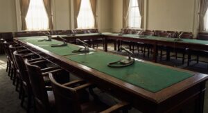 Empty hearing room with long tables, microphones, and chairs arranged for a formal meeting