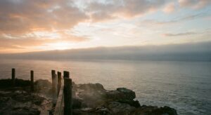 Rocky coastline with calm sea and a low cloud layer near the horizon at sunset