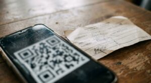 Smartphone displaying a QR code lying on a wooden table next to a handwritten note