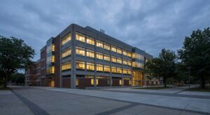 Exterior view of a research institute building at dusk, lit windows and empty plaza.