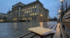 Exterior of a stone parliamentary building at dusk with an unbranded folder on a bench suggesting public inquiry.