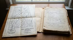 Close-up of a county map of Alabama with a folded medical chart on a table, indicating geographic and medical context.