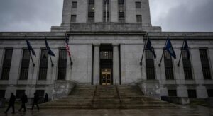 Government building facade with flags and steps, implying regulatory or legal action.