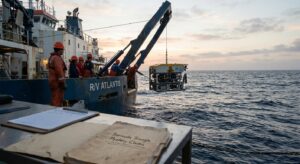 Research vessel crew launching an ROV at dawn, instruments and evidence folder on deck.