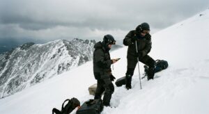 Two researchers measuring slope angle on stepped snow terrain with probes and GPS equipment.