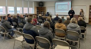 Parents and a school official in a neutral community meeting setting discussing online safety.