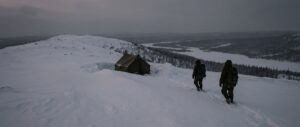 Snowy Ural ridge at dusk with a solitary tent and people walking near the tree line.